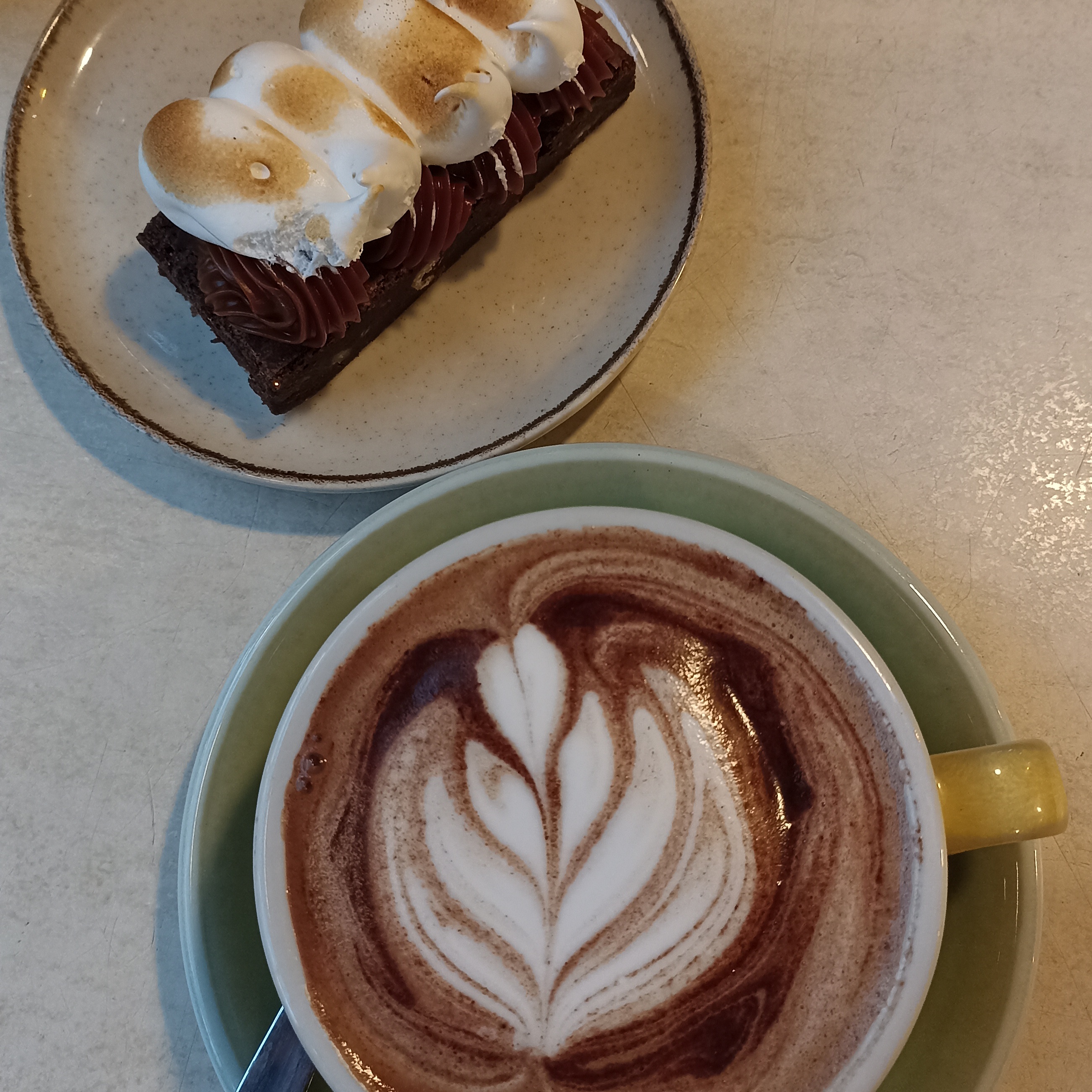 Imagen donde se muestra un brownie nevado junto a una taza de chocolate caliente, cafetería Ritual